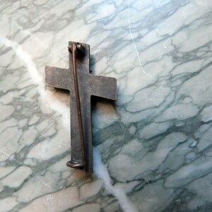 May include: A silver-toned cross pin with a pin back. The cross is slightly raised and has a textured surface.