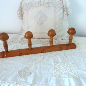 Peut inclure: Un porte-manteau en bois avec quatre crochets. Le porte-manteau est en bois brun clair et a une finition naturelle. Les crochets sont ronds et ont un sommet légèrement en forme de champignon.