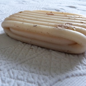 May include: A close-up of a white, ribbed bar of soap with brown spots and flecks of gold glitter.