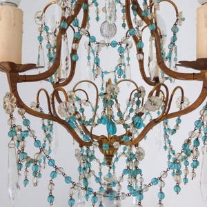 May include: Ornate gold-toned chandelier with clear and turquoise beaded strands and crystal accents. The fixture features curved arms and decorative floral elements, creating an elegant and vintage aesthetic. Includes two light bulbs.