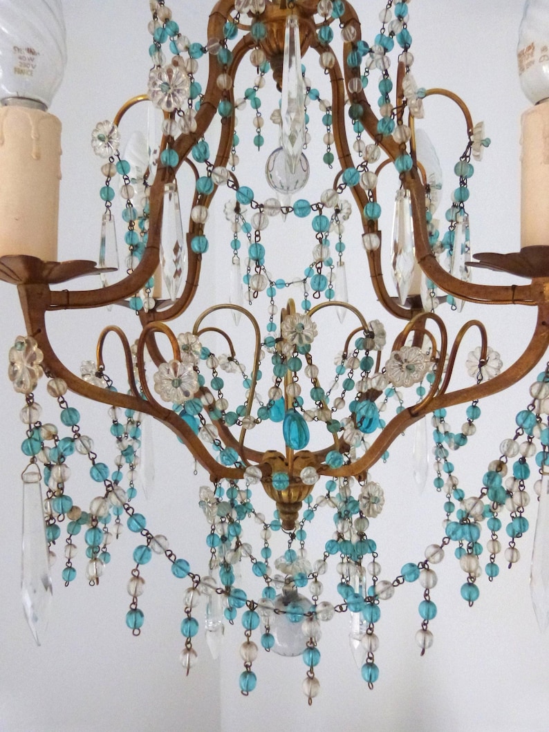May include: Ornate gold-toned chandelier with clear and turquoise beaded strands and crystal accents. The fixture features curved arms and decorative floral elements, creating an elegant and vintage aesthetic. Includes two light bulbs.
