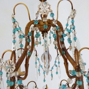 May include: Ornate, antique chandelier with a gold-toned frame. It features clear crystal pendants and strands of turquoise and clear beads. The design includes floral accents and curved arms, creating an elegant, vintage aesthetic.