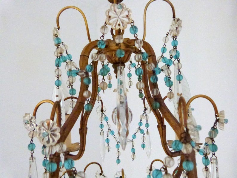 May include: Ornate, antique chandelier with a gold-toned frame. It features clear crystal pendants and strands of turquoise and clear beads. The design includes floral accents and curved arms, creating an elegant, vintage aesthetic.