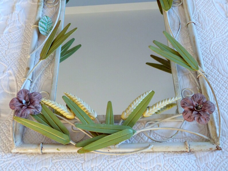 May include: A white metal mirror with a floral design. The mirror is decorated with green leaves, yellow wheat stalks, and pink flowers.