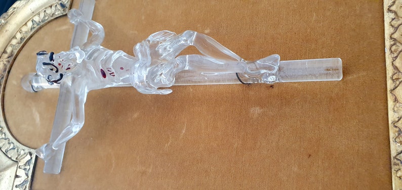 May include: A clear glass crucifix with a depiction of Jesus Christ. The figure is detailed with red paint to represent blood.
