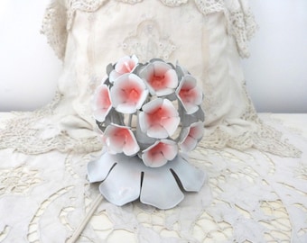 May include: A vintage metal flower sculpture with a bouquet of pink and white blossoms. The flowers are arranged in a spherical shape, supported by a gray, petal-shaped base. The sculpture is a decorative piece.