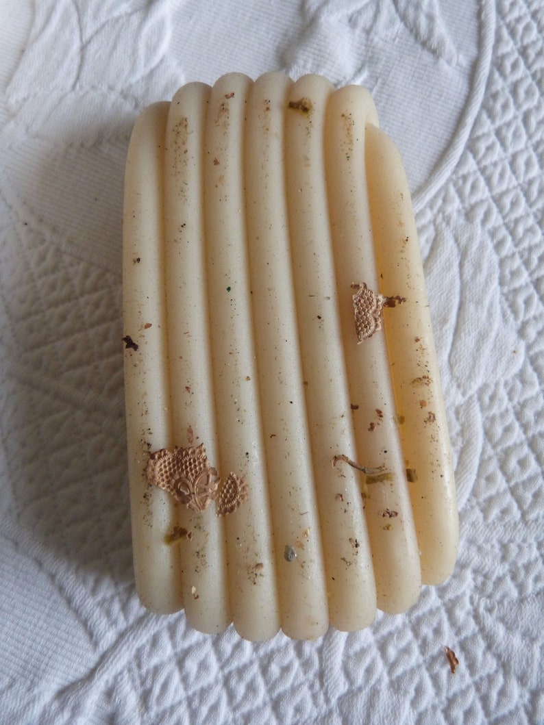 May include: A close-up of a beige, cylindrical candle with a textured surface. The candle is made of multiple layers of wax, creating a striped pattern. The candle has a few small, brown pieces of debris on its surface.