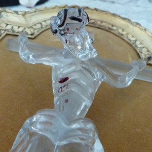 May include: A glass sculpture of a figure on a cross. The figure is clear glass with red accents. The sculpture is framed in a gold-colored frame.