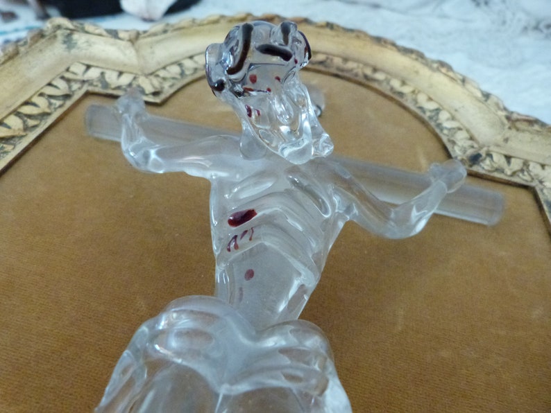 May include: A glass sculpture of a figure on a cross. The figure is clear glass with red accents. The sculpture is framed in a gold-colored frame.