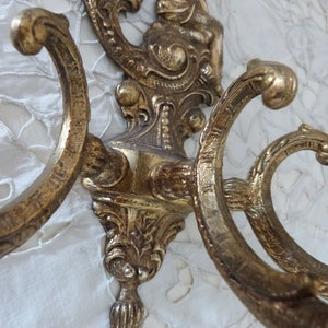 K&ouml;nnte beinhalten: Verzierter Wandhaken aus goldfarbenem Metall mit drei Haken und einer dekorativen Cherubfigur oben.