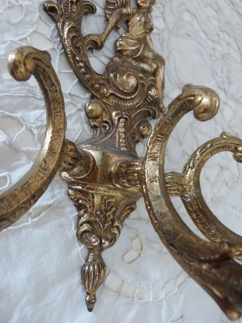 K&ouml;nnte beinhalten: Verzierter Wandhaken aus goldfarbenem Metall mit drei Haken und einer dekorativen Cherubfigur oben.