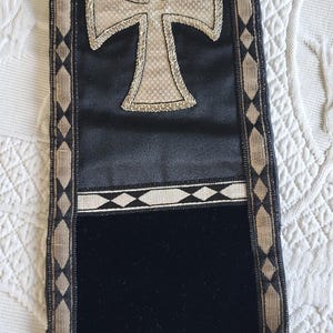 May include: Black and gold religious stole with a large cross design. The stole features a black velvet panel, gold trim, and a decorative fringe. The cross is embroidered with a gold-colored thread.
