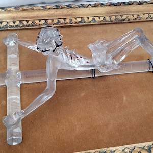 May include: A clear glass sculpture of a person on a cross, framed in a gold ornate frame.