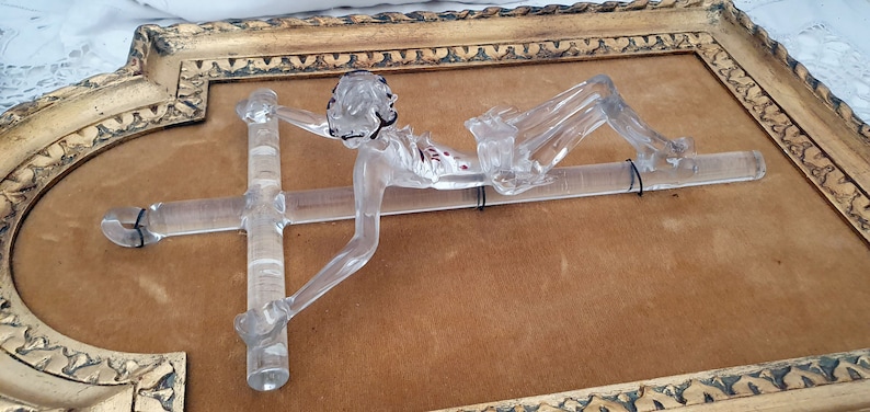 May include: A clear glass sculpture of a person on a cross, framed in a gold ornate frame.