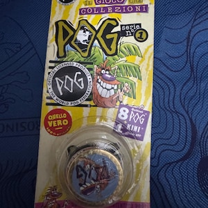 Può includere: Un set di giochi POG vintage, con un oggetto da collezione della serie 1. La confezione è gialla con la parola "POG" a grandi lettere. Il set include diversi POG con disegni di personaggi dei cartoni animati.