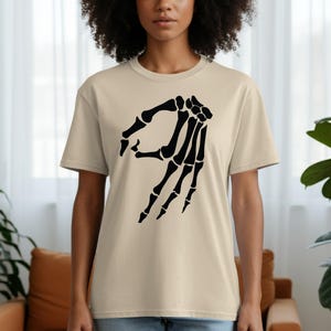 Tan t-shirt with black skeleton hand making the 'okay' gesture.