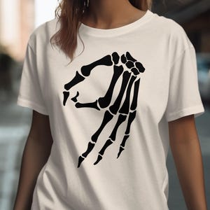 White t-shirt with black skeleton hand making the "okay" gesture.