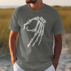 Grey t-shirt with white skeleton hand making "okay" gesture on a beach.