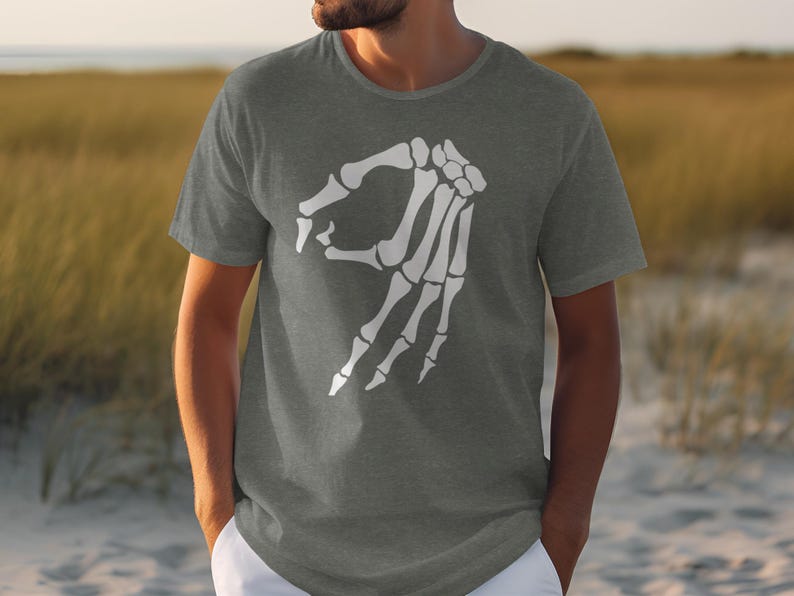 Grey t-shirt with white skeleton hand making "okay" gesture on a beach.