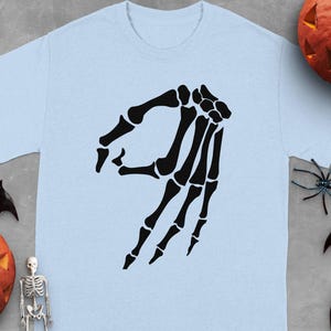 Light blue t-shirt with a black skeleton hand making the OK sign.