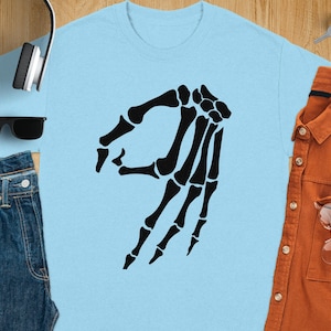 Light blue t-shirt with black skeleton hand pointing gesture.
