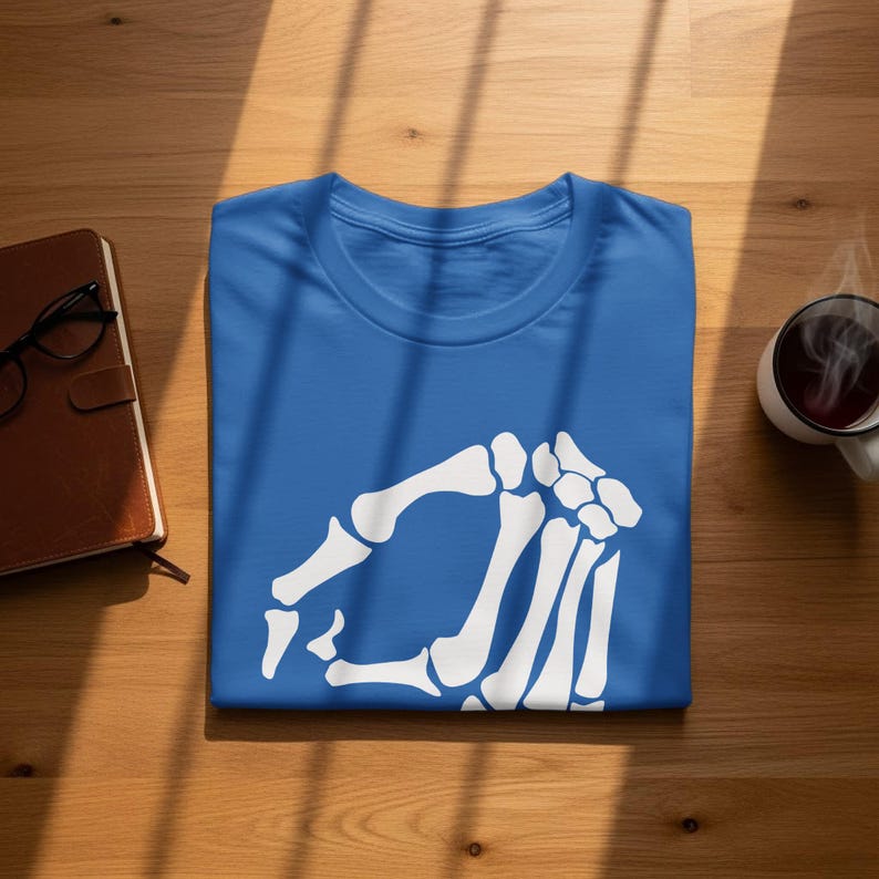 Blue t-shirt with a white skeleton hand graphic, laid flat on a wooden surface.