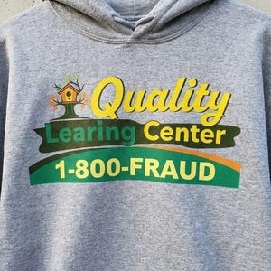 Könnte beinhalten: Grauer Kapuzenpullover mit dem Schriftzug "Quality Learning Center" in Gelb und Grün sowie einer Vogelhaus-Grafik. Der Schriftzug "1-800-FRAUD" ist unter dem zentralen Text aufgedruckt.