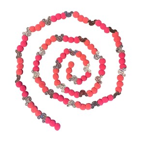 Könnte beinhalten: Eine spiralförmige Girlande aus rosa und korallenfarbenen Filzkugeln, durchsetzt mit glitzernden Mickey Mouse-Kopf-Akzenten. Die Girlande ist auf weißem Hintergrund angeordnet und erzeugt ein dekoratives und verspieltes Design.