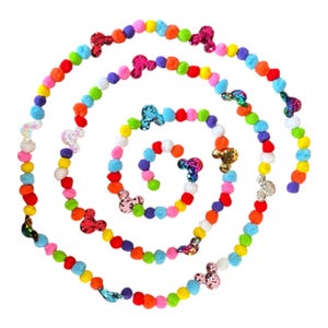 Puede incluir: Una guirnalda en espiral de pompones multicolores, rojos, naranjas, amarillos, verdes, azules y rosas. La guirnalda está adornada con formas de cabeza de Mickey Mouse con lentejuelas en varios colores, creando un diseño festivo y lúdico.