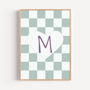 Könnte beinhalten: Gerahmter Druck mit einem Schachbrettmuster in Weiß und einem gedämpften Blaugrün. Ein weißes Herz mit dem lila Buchstaben "M" ist mittig auf dem Design platziert. Der Rahmen hat eine helle Holzfarbe.