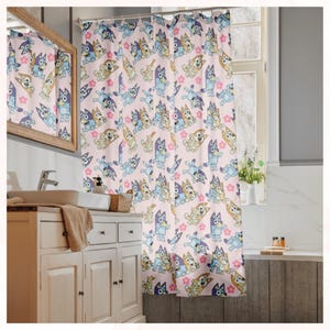 Puede incluir: Una cortina de ducha rosa con un patr&oacute;n repetido de perros de dibujos animados en varias poses, con acentos en azul claro, beige y morado. El dise&ntilde;o incluye formas de flores rosas. La cortina est&aacute; en un ba&ntilde;o.