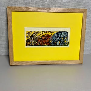 May include: A framed art print with a yellow mount and a rectangular image of stylized animals. The animals include a giraffe, tiger, and elephant. The frame is made of light-coloured wood.