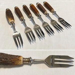 May include: A set of six silver-toned metal forks with textured brown antler-style handles. Each fork features three tines and is stamped with the word ISRAEL on the metal neck. The design includes a decorative silver collar between the handle and fork.