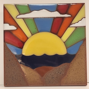 Puede incluir: Azulejo de cerámica cuadrado con un diseño de puesta de sol colorido. El sol es amarillo, con rayos rojos, naranjas, verdes y amarillos. Nubes blancas están dispersas en un cielo azul. La parte inferior del azulejo representa un mar azul oscuro y tierra marrón.