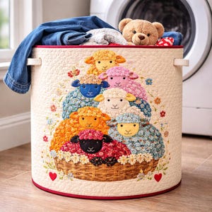 May include: A round, cream laundry hamper with a red trim and white handles. It features an appliqué design of colourful sheep in a basket, surrounded by flowers. The hamper is filled with blue jeans, a grey towel, and a teddy bear.