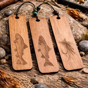 May include: Three wooden bookmarks with black cords and decorative beads. Each bookmark features an engraved design: two with fish and one with a fishing fly. The bookmarks are displayed on a rustic wooden surface with fishing gear.