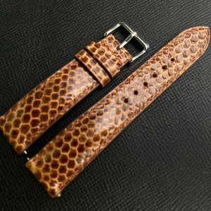 May include: A two-piece watch strap featuring a textured, brown snakeskin pattern with a glossy finish. The strap includes a silver-toned metal buckle and two matching leather keepers, with visible stitching along the edges of the band.