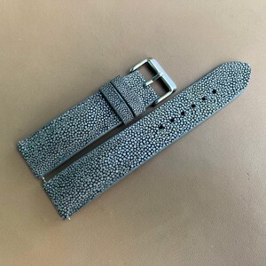 May include: A two-piece watch strap featuring a textured grey surface with a distinct speckled pattern. The strap includes a silver-toned metal buckle and a matching sliding loop, with multiple circular holes punched along the length of the band.