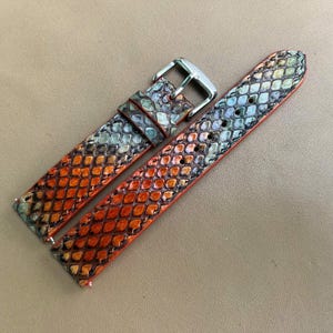 May include: A two-piece watch strap featuring a textured snakeskin pattern with a gradient of vibrant orange, deep red, and muted grey tones. The strap includes a polished silver-tone metal buckle and a matching sliding keeper loop for secure fastening.