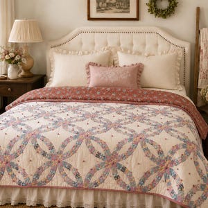 May include: A cream-colored quilt featuring a double wedding ring pattern with floral fabric in shades of blue, pink, and green. The quilt has small tufted knots at the intersections and is draped over a bed with a white tufted headboard.