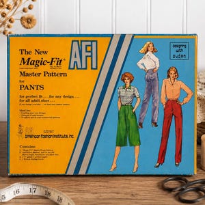 May include: A rectangular box for The New Magic-Fit Master Pattern for PANTS by AFI. The box is yellow and blue with illustrations of three figures wearing different pant styles, including green culottes, blue jeans, and red trousers.