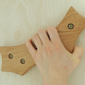 May include: A light brown wooden handle with three screws. The handle has a curved, ergonomic design. The wood grain is visible. The handle is held in a hand.