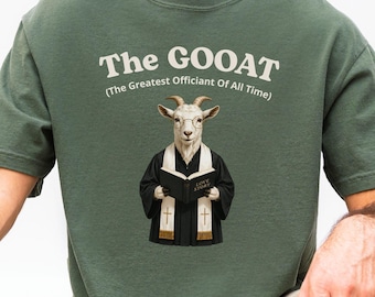 May include: A forest green short-sleeved t-shirt featuring a graphic of a goat dressed as an officiant holding a book. The text above the goat reads The GOOAT and below it reads The Greatest Officiant Of All Time in white lettering.