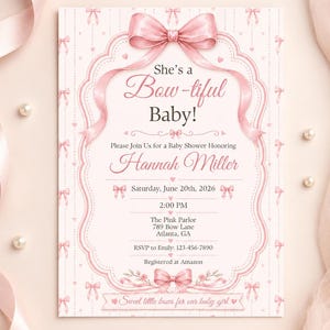 May include: A rectangular baby shower invitation card featuring a large pink bow at the top and bottom, with a decorative scalloped frame. The text reads: She's a Bow-tiful Baby! Please Join Us for a Baby Shower Honoring Hannah Miller, Saturday, June 20th, 2026, 2:00 PM, The Pink Parlor, 789 Bow Lane, Atlanta, GA, RSVP to Emily: 123-456-7890, Registered at Amazon, Sweet little bows for our baby girl.
