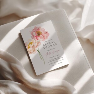 Pu&ograve; includere: Un biglietto d'invito per un addio al nubilato con fiori ad acquerello rosa e crema. Il biglietto include il testo "Bridal Shower" e il nome "Shelly Bridges". L'invito &egrave; posto su uno sfondo neutro.