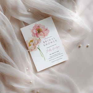Pu&ograve; includere: Un invito per un addio al nubilato con arte floreale ad acquerello in rosa e giallo. L'invito &egrave; su una carta bianca con testo in un carattere delicato. La carta &egrave; posta su un tessuto trasparente di colore chiaro con perle sparse.