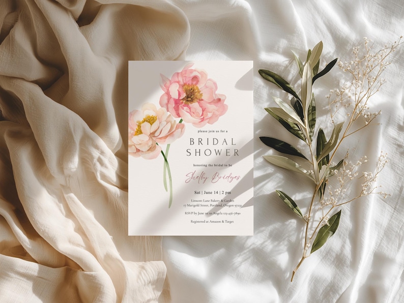 Pu&ograve; includere: Un invito per un addio al nubilato con peonie rosa ad acquerello. L'invito include il testo "BRIDAL SHOWER" e i dettagli dell'evento. &Egrave; posto su una superficie bianca, accompagnato da rami di ulivo e tessuto morbido.