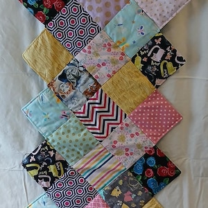 May include: A quilted, patchwork table runner featuring a variety of patterned fabrics. The design includes squares with floral, geometric, and animal prints in colors like pink, blue, yellow, and black. The runner is approximately 40 inches long.