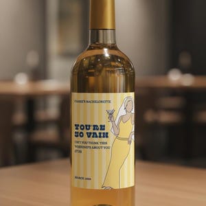May include: A wine bottle with a gold cap and a label that reads "CASSIE'S BACHELORETTE" with the text "YOU'RE SO VAIN". The label features a yellow and white striped background and an illustration of a woman in a yellow dress holding a cocktail.
