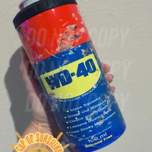 Puede incluir: Un aislante de bebidas cilíndrico con tapa roja y base azul, con el logotipo de WD-40 e información del producto. El diseño imita una lata de WD-40, con un borde negro en la parte superior. Capacidad: 100 ml.